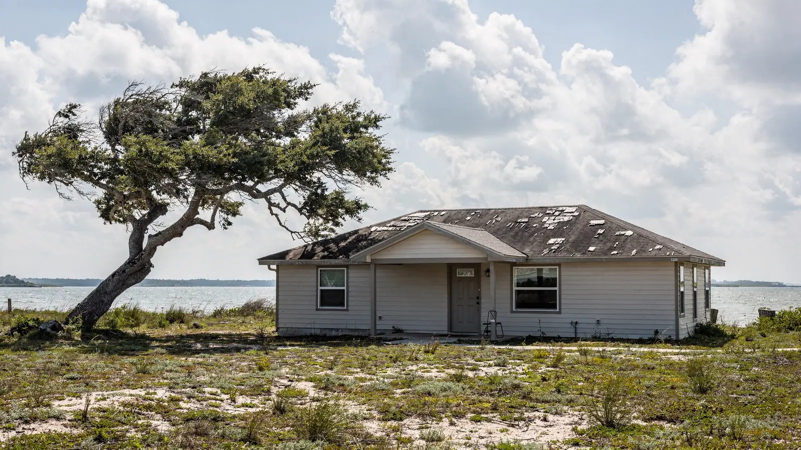 A low house near the water with a weathered grey shingle roof under a wide coastal sky.