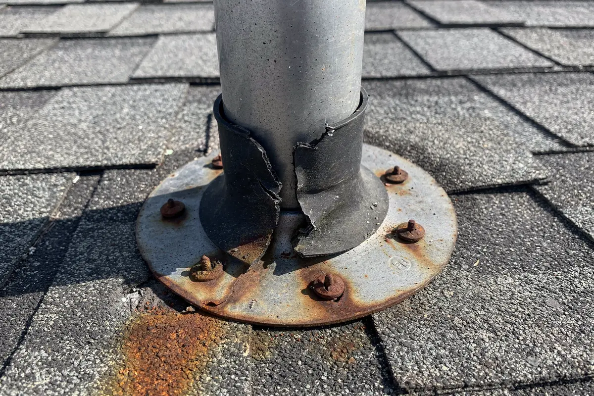 A metal vent collar on a roof with rust bleeding from the fasteners below it and corrosion around the base.